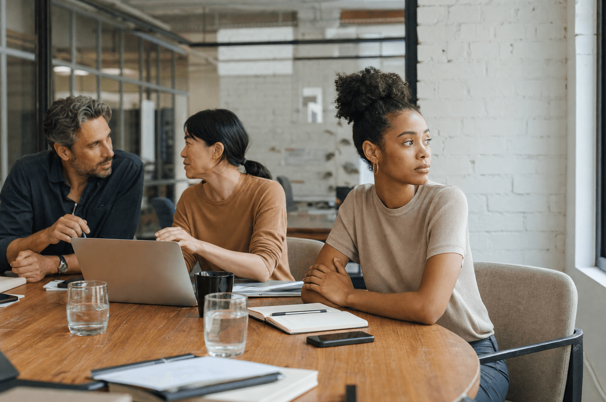 A meeting scene where one participant has visibly checked out while colleagues continue the conversation.